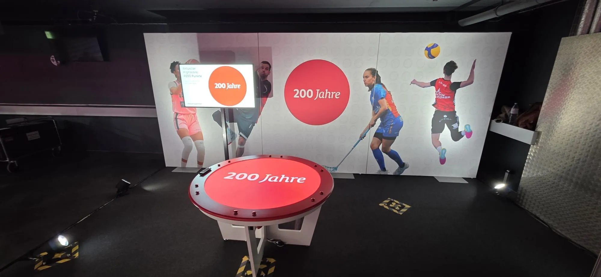 Round LED gaming table with «200 Jahre» lettering in front of an indoor-sports photo wall and Mobiliar anniversary logo, with a high-score screen to the left