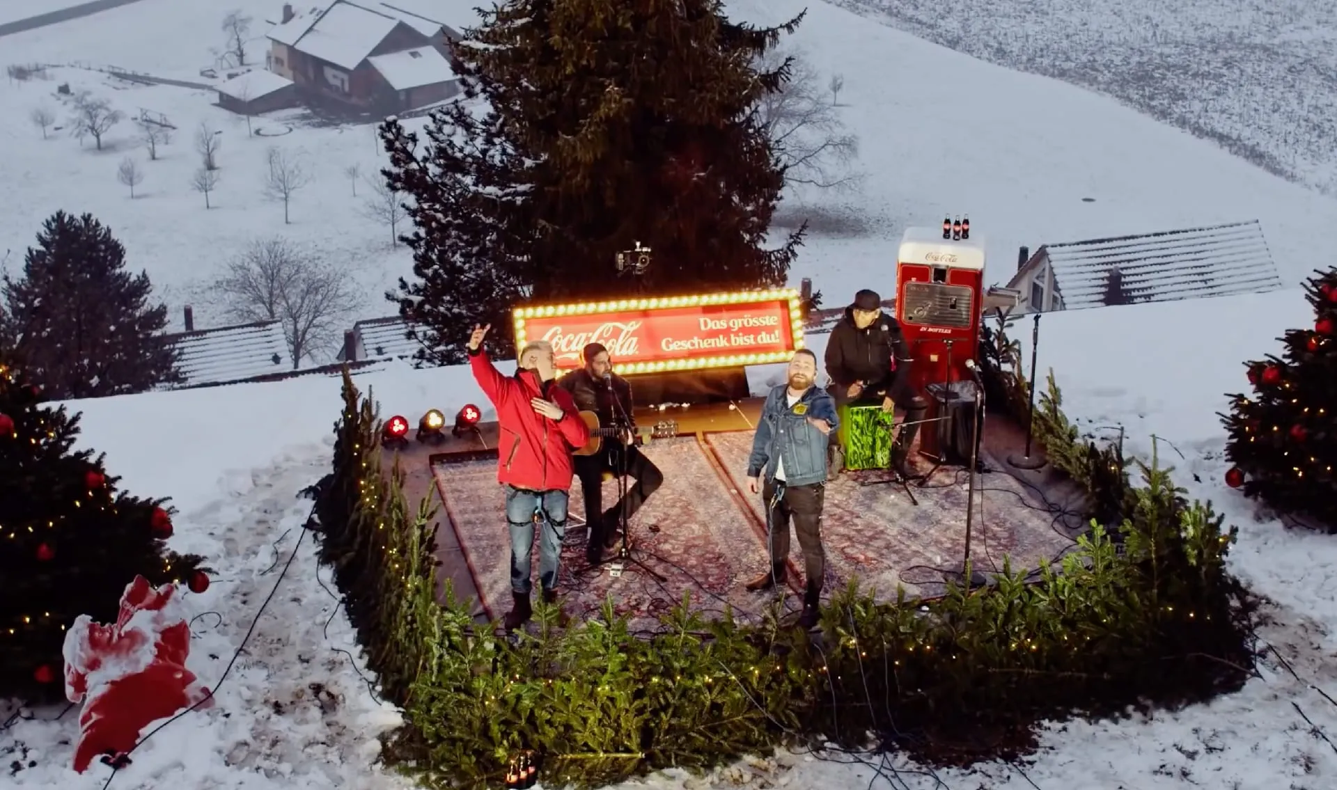 Three musicians on a stage in the snow with a red Coca-Cola illuminated sign, Christmas trees and a vintage drinks machine